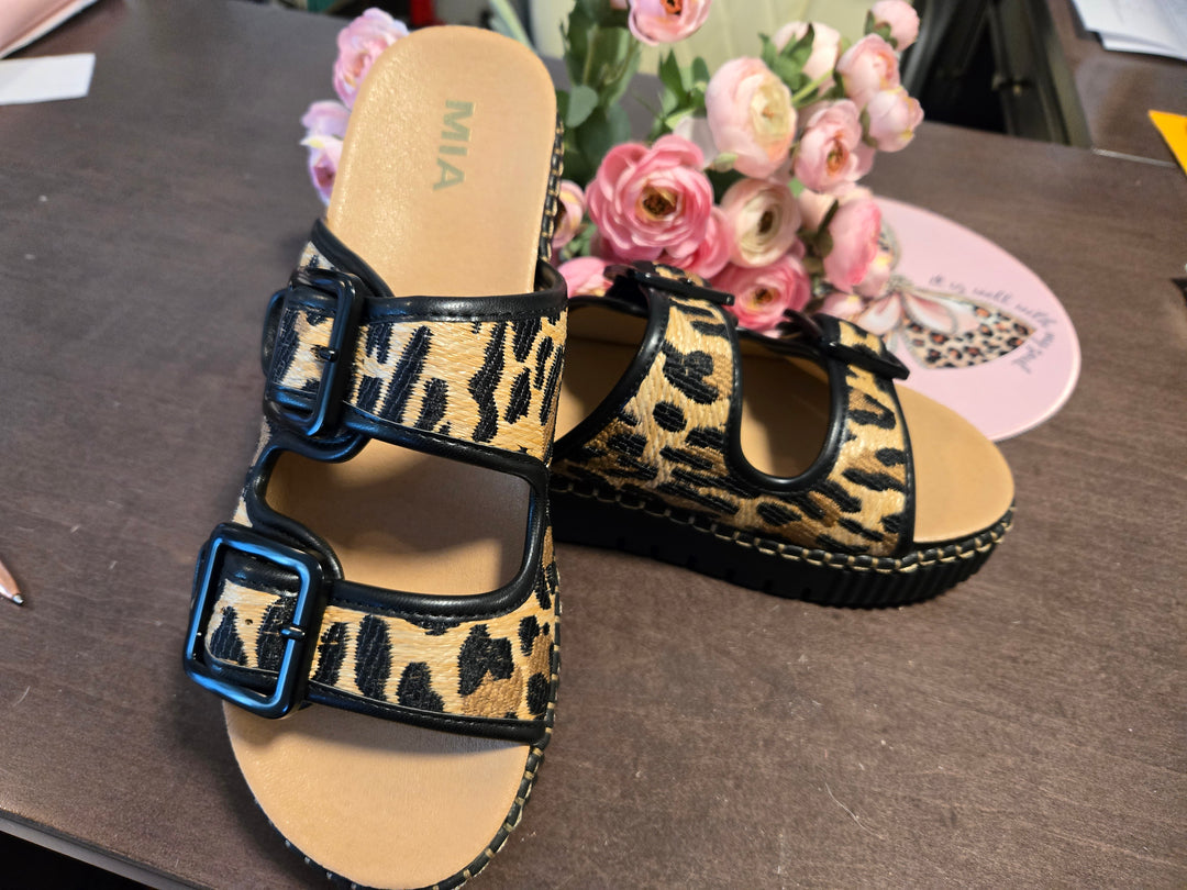 Leopard print sandals with blue buckles on a table with flowers in the background